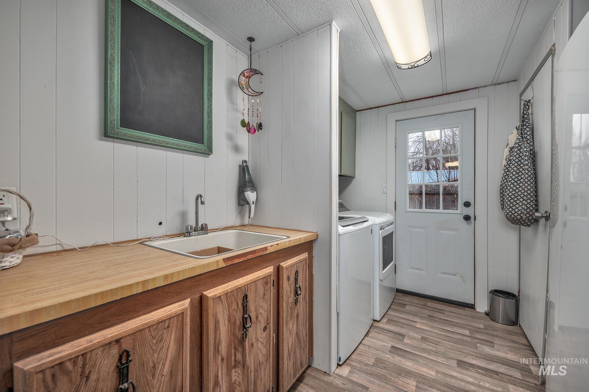 1165 Pioneer Road Weiser, ID 83672 - Photo 23 of 24 Washroom featuring cabinet space, light wood-style flooring, washing machine and dryer, wooden walls, and a textured ceiling