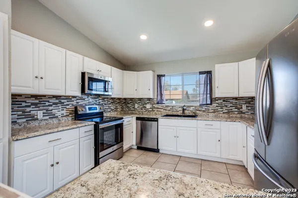a kitchen with granite countertop a sink a stove a refrigerator and white cabinets