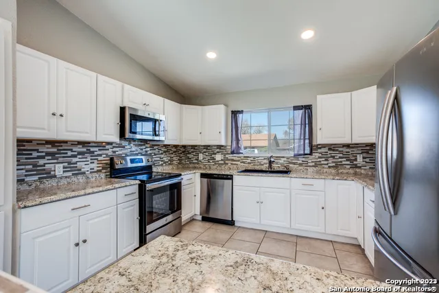 a kitchen with granite countertop a sink a stove a refrigerator and white cabinets