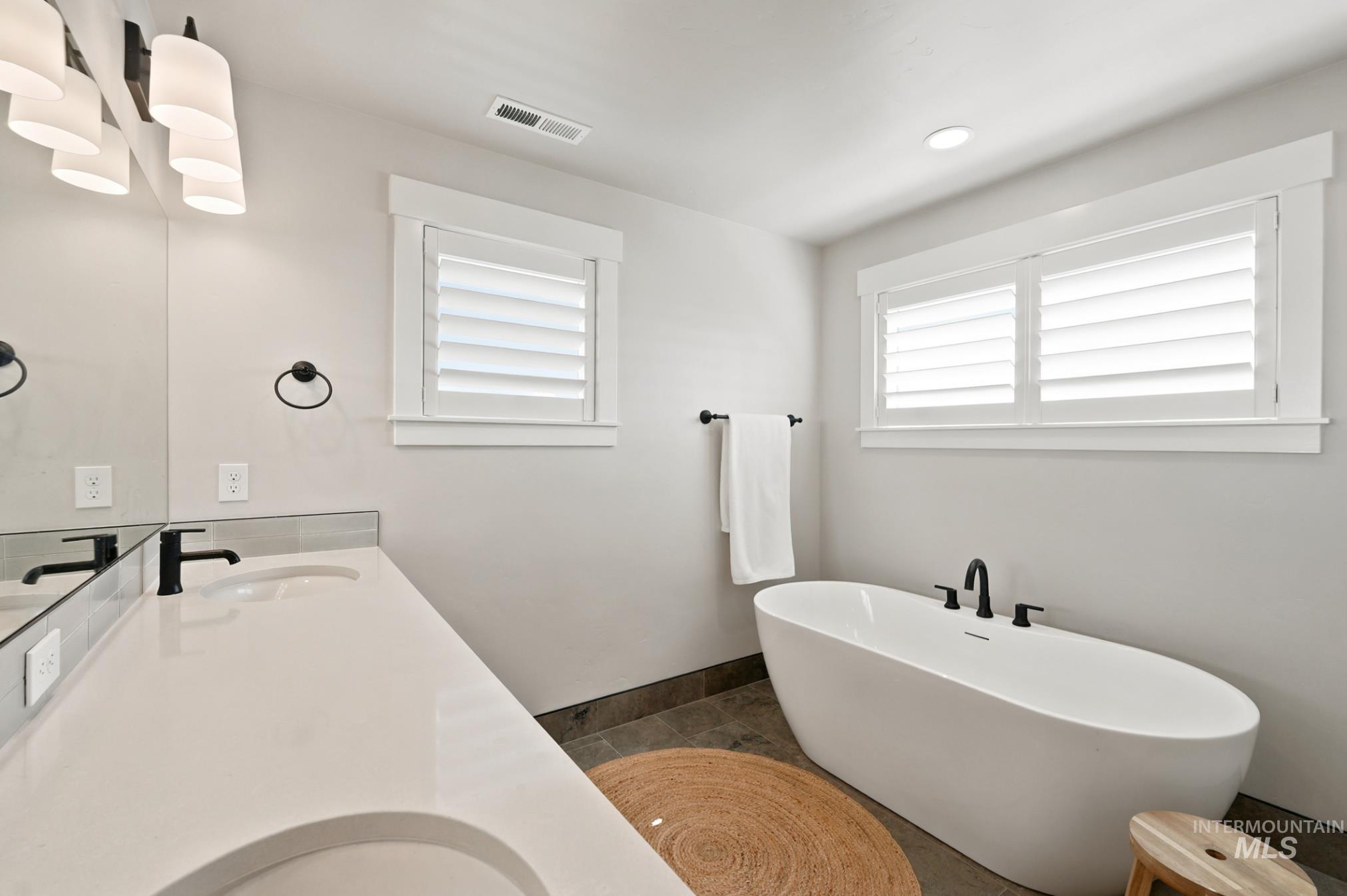 6933 South Zenith Avenue Meridian, ID 83642 - Photo 29 of 34 Bathroom featuring a white freestanding soaking tub with matte black fixtures, a dual vanity with light countertops and undermount sinks, and windows with white plantation shutters