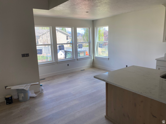 4676 West 75 North, Unit 401 West Point, UT 84015 - Photo 4 of 17 Open-concept living area featuring a light wood-finish flooring, a series of three large windows, a built-in kitchen island with a light-toned countertop, and white baseboards