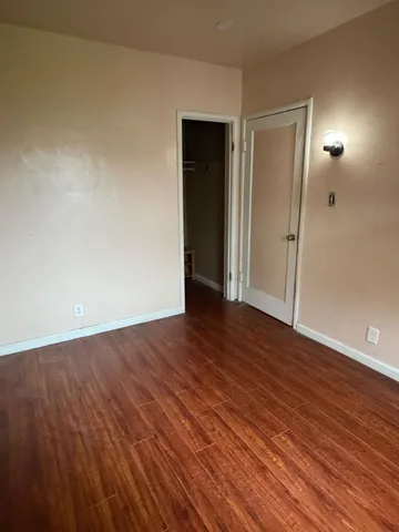 a view of an empty room with wooden floor and a mirror