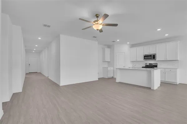 a view of an empty room with kitchen and wooden floor