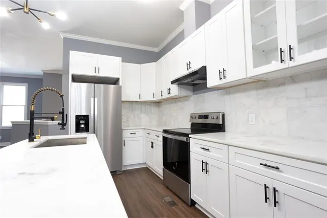 a kitchen with stainless steel appliances kitchen island granite countertop a refrigerator a sink dishwasher a stove and white cabinets with wooden floor