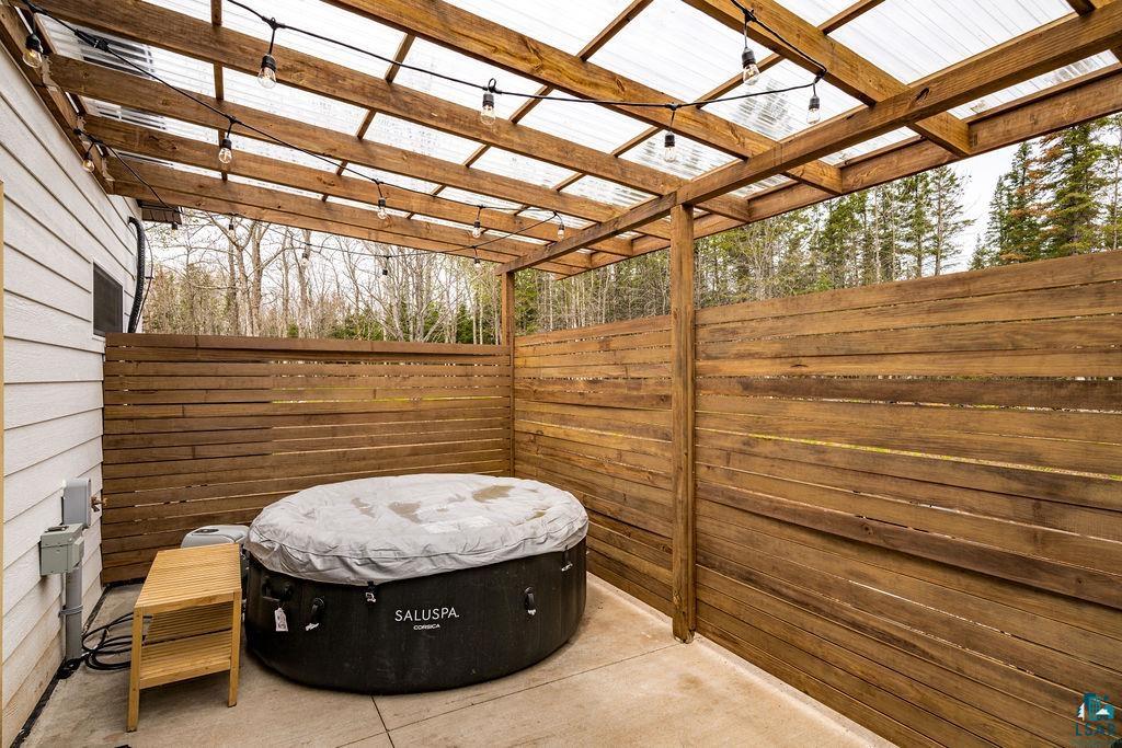 1825 East Shilhon Road Duluth, MN 55804 - Photo 35 of 37 Outdoor patio featuring a hot tub, concrete flooring, slatted wood privacy fencing and a clear panel roof supported by a wood frame.