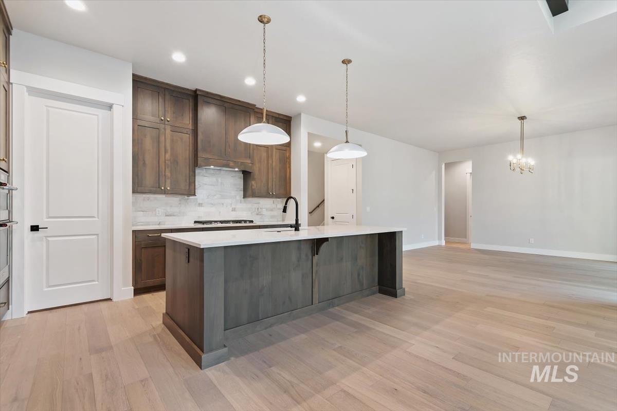 2147 East Blakehurst Avenue Kuna, ID 83634 - Photo 10 of 43 Kitchen featuring decorative backsplash, decorative light fixtures, a kitchen breakfast bar, light stone countertops, and light wood finished floors