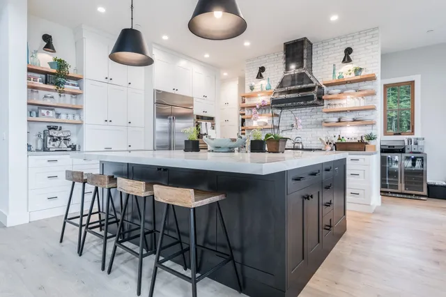 a kitchen with stainless steel appliances a sink a stove a refrigerator and chairs