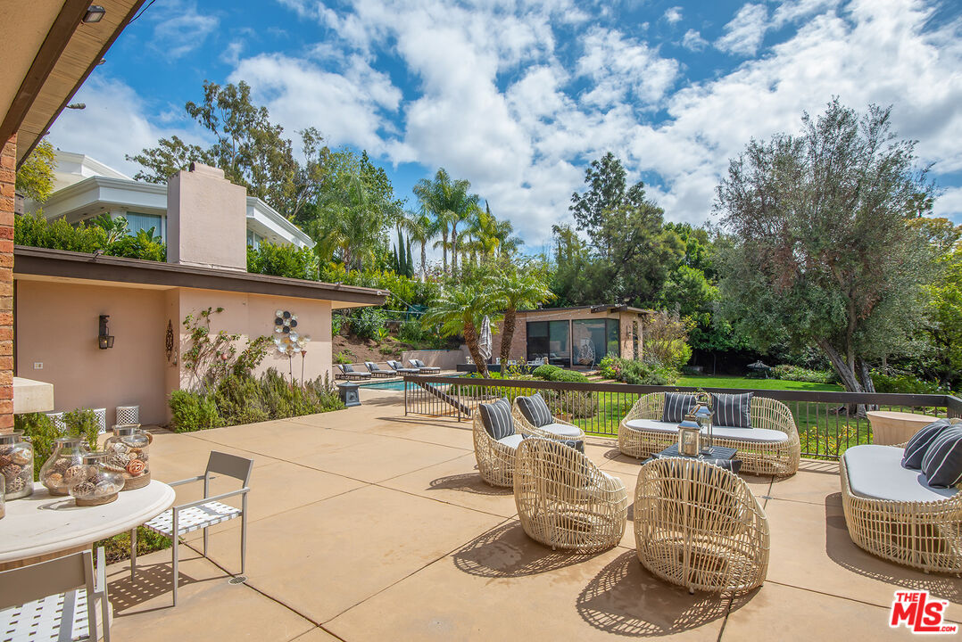 1018 Summit Drive Beverly Hills, CA 90210 - Photo 19 of 21 a view of a patio with couches table and chairs potted plants and a palm tree
