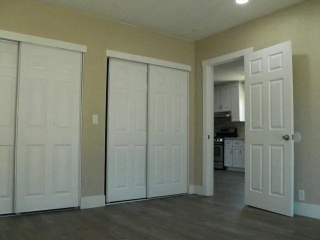 an empty room with wooden floor closet and windows