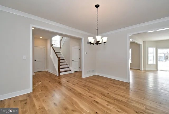 a view of an empty room with wooden floor staircase and a chandelier