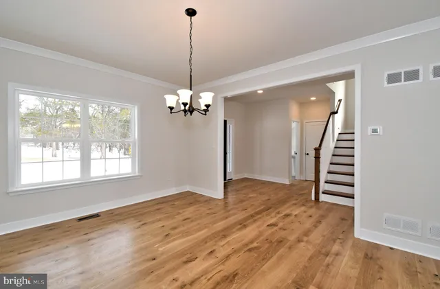 a view of an empty room with wooden floor stairs and a chandelier