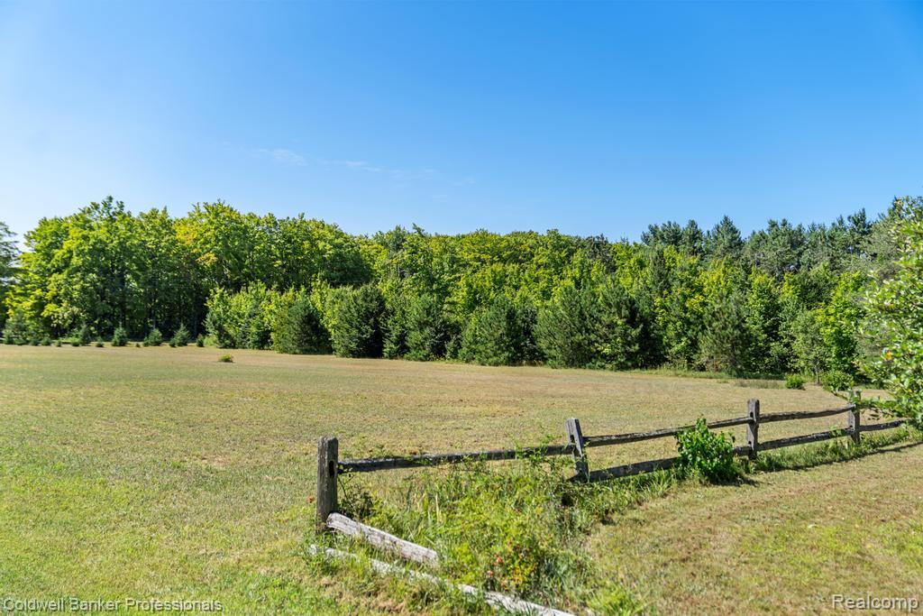 6389 Postlewait Road Mancelona, MI 49659 - Photo 49 of 50 Expansive grassy field with a rustic split-rail fence, bordered by a dense line of mature trees