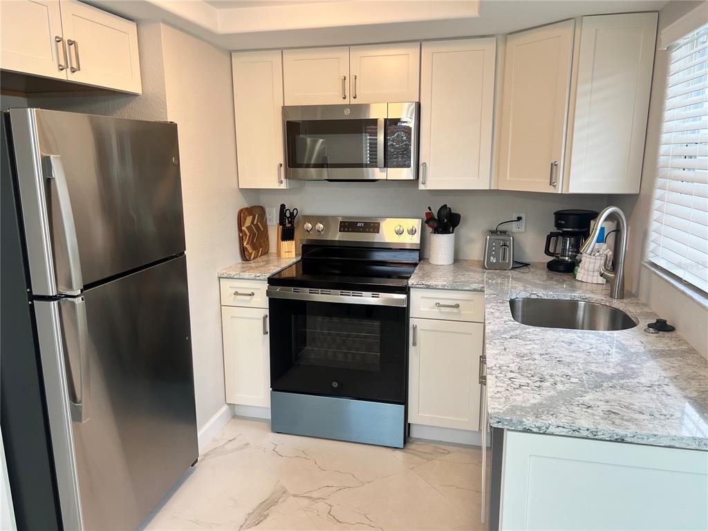 6154 Midnight Pass Road, Unit B14 Sarasota, FL 34242 - Photo 4 of 15 a kitchen with granite countertop a refrigerator stove and microwave