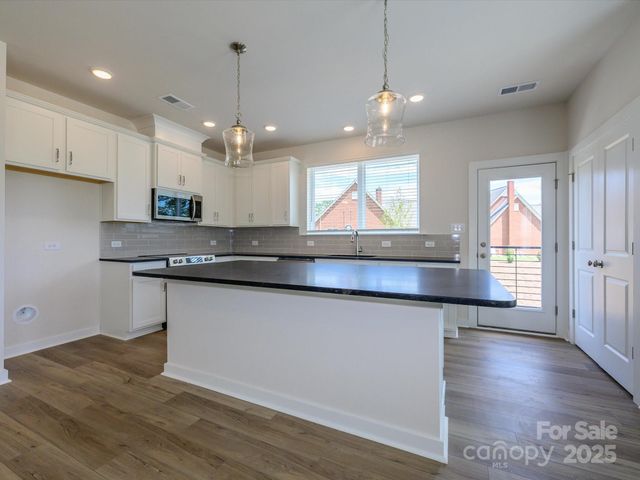 a kitchen with stainless steel appliances granite countertop wooden floors white cabinets and window