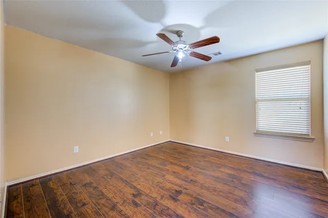 an empty room with wooden floor fan and windows