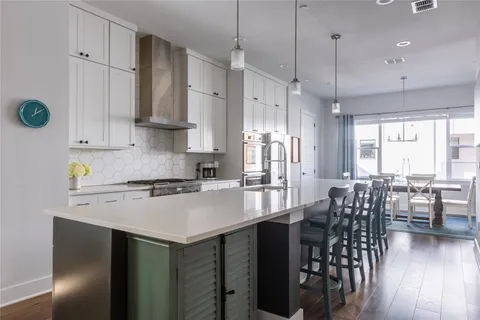 a kitchen with stainless steel appliances granite countertop a stove a refrigerator a kitchen island a dining table and chairs with wooden floor