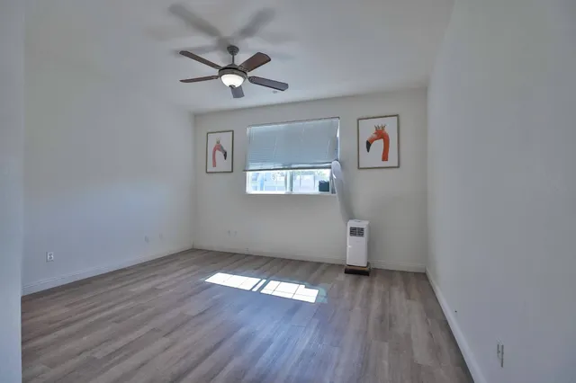 an empty room with wooden floor chandelier fan and windows