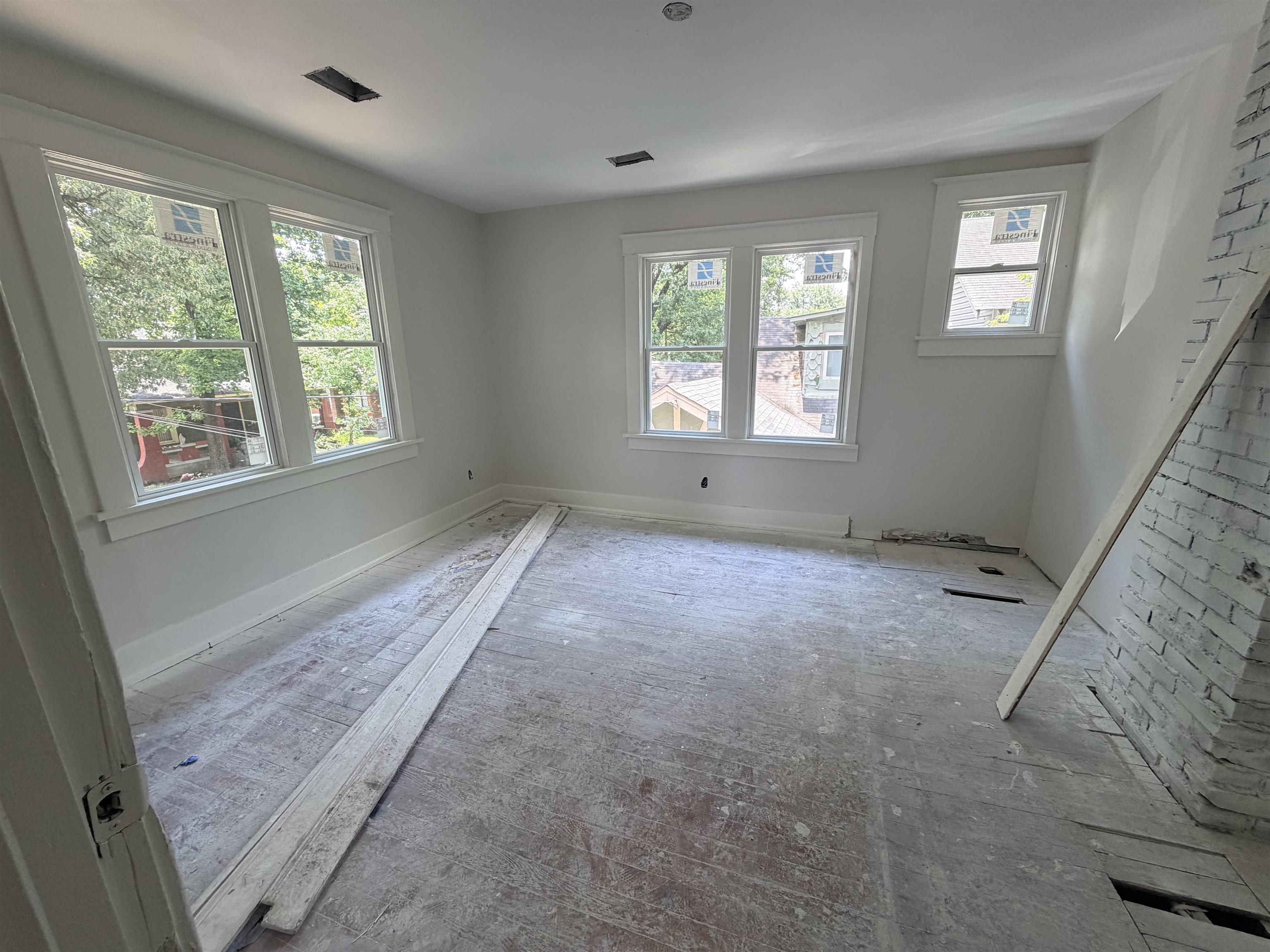 961 Meda Street Memphis, TN 38104 - Photo 20 of 27 Room featuring multiple windows, painted white walls, white trim, exposed flooring, and a painted brick accent wall