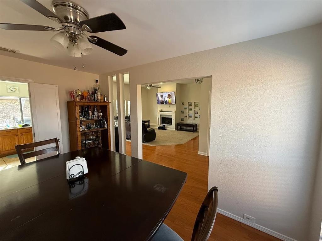 6505 Mc Cormick Ranch Court Plano, TX 75023 - Photo 5 of 21 Dining area featuring a ceiling fan with light fixture, wood-finish flooring, and a broad pass-through opening to an additional living space with a fireplace