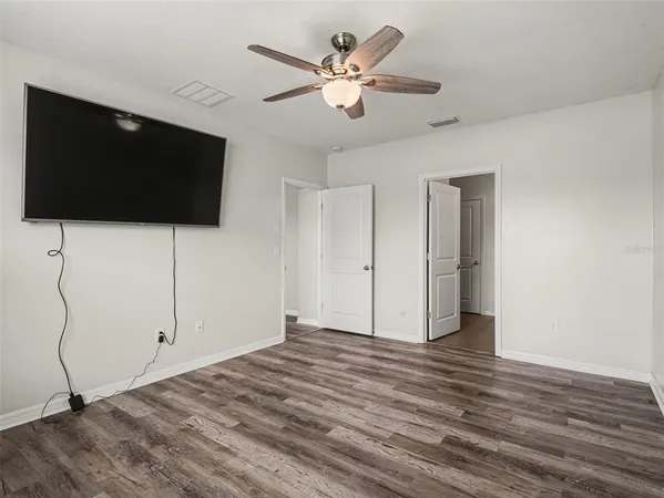 a view of an empty room with wooden floor and a ceiling fan