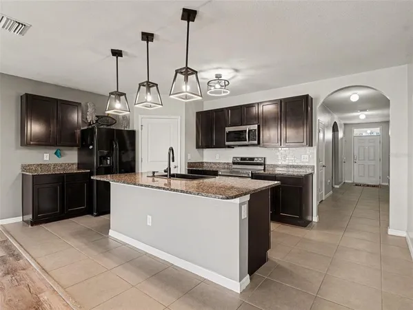 a kitchen with stainless steel appliances kitchen island granite countertop a stove top oven a sink dishwasher a refrigerator and a fireplace with wooden floor
