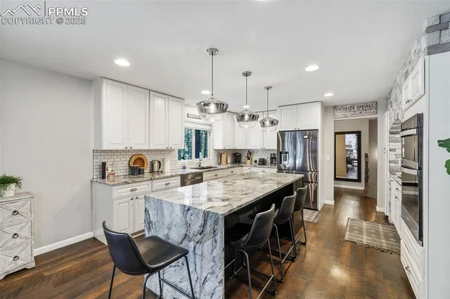 a kitchen with stainless steel appliances kitchen island granite countertop a table chairs and a refrigerator