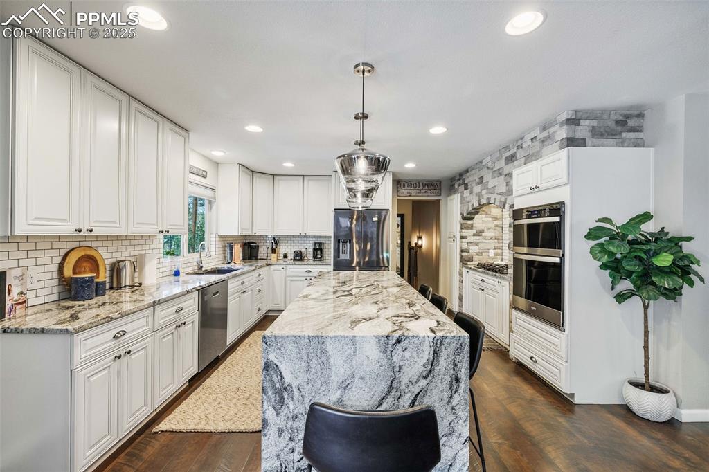6940 Franciville Road Colorado Springs, CO 80908 - Photo 10 of 40 a large kitchen with kitchen island granite countertop a stove a sink dishwasher and white cabinets with wooden floor