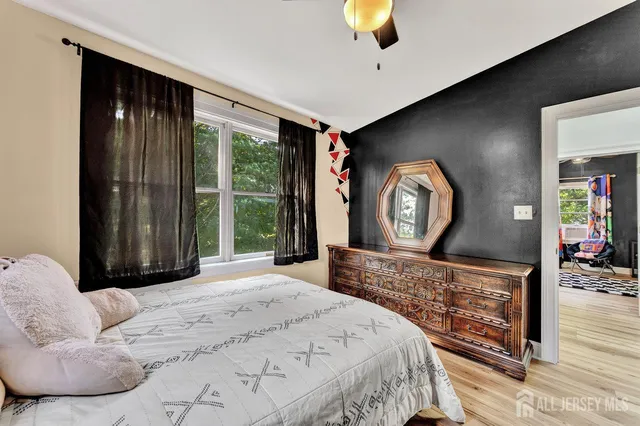 a bedroom with a bed a mirror on dresser and a large window