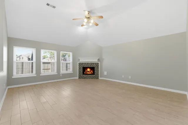 a view of an empty room with wooden floor fireplace and a window