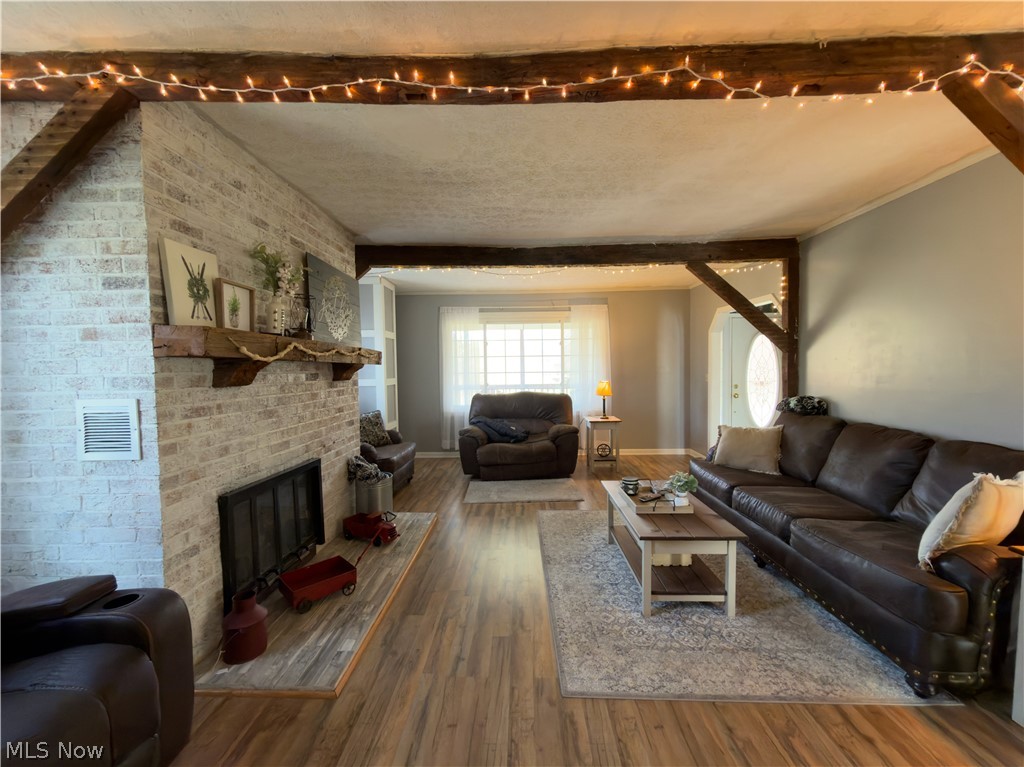 17377 Murphy Road Amesville, OH 45711 - Photo 12 of 43 Living room featuring a fireplace, wood finished floors, brick wall, beam ceiling, and ornamental molding