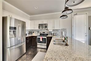 2947 Moss Street Austin, TX 78722 - Photo 6 of 15 Kitchen featuring appliances with stainless steel finishes, white cabinets, decorative backsplash, a peninsula, and pendant lighting