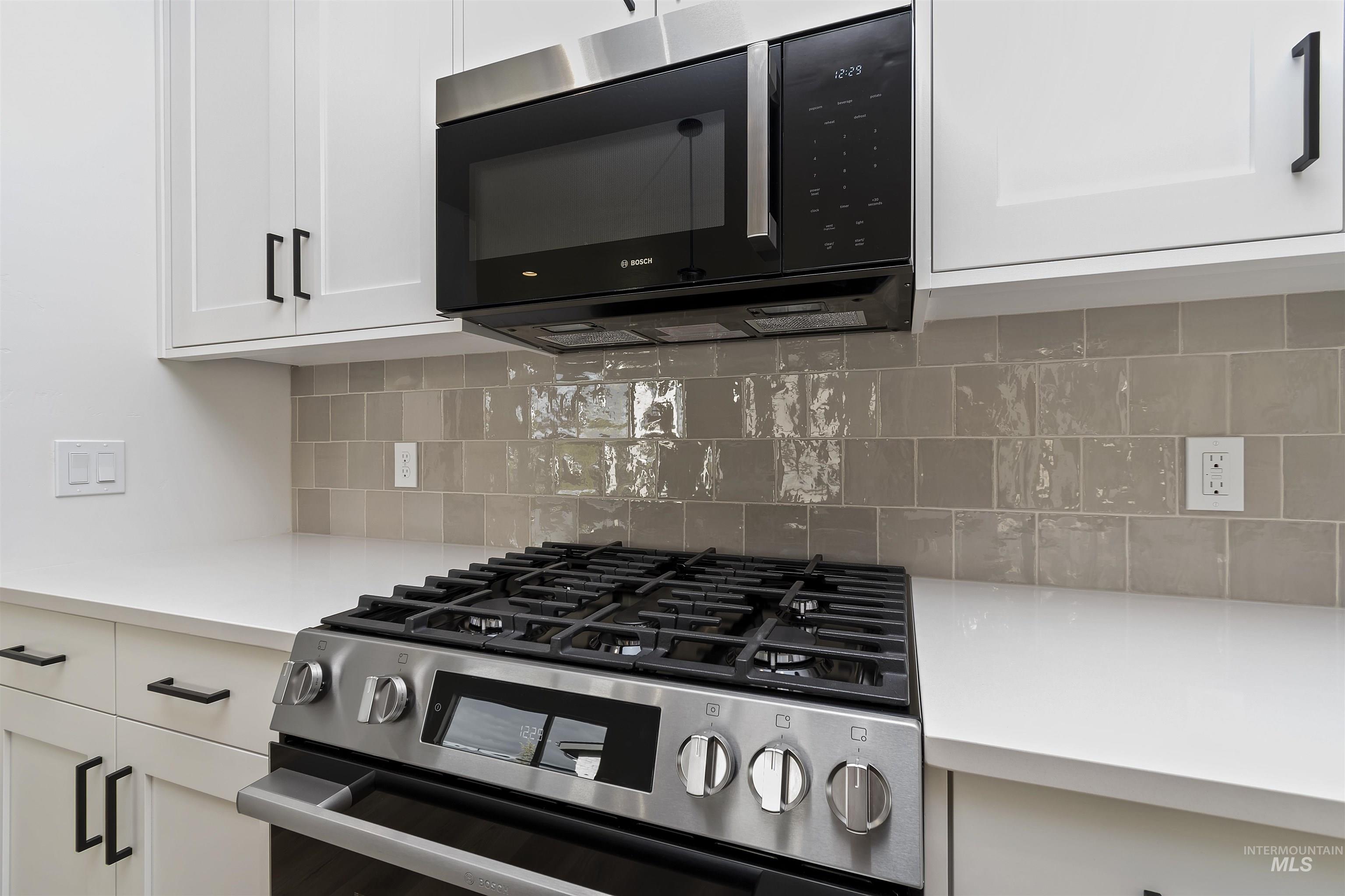 764 South Calhoun Lane Star, ID 83669 - Photo 13 of 48 Kitchen view of stainless steel range with gas cooktop, white cabinetry, black microwave, and decorative backsplash