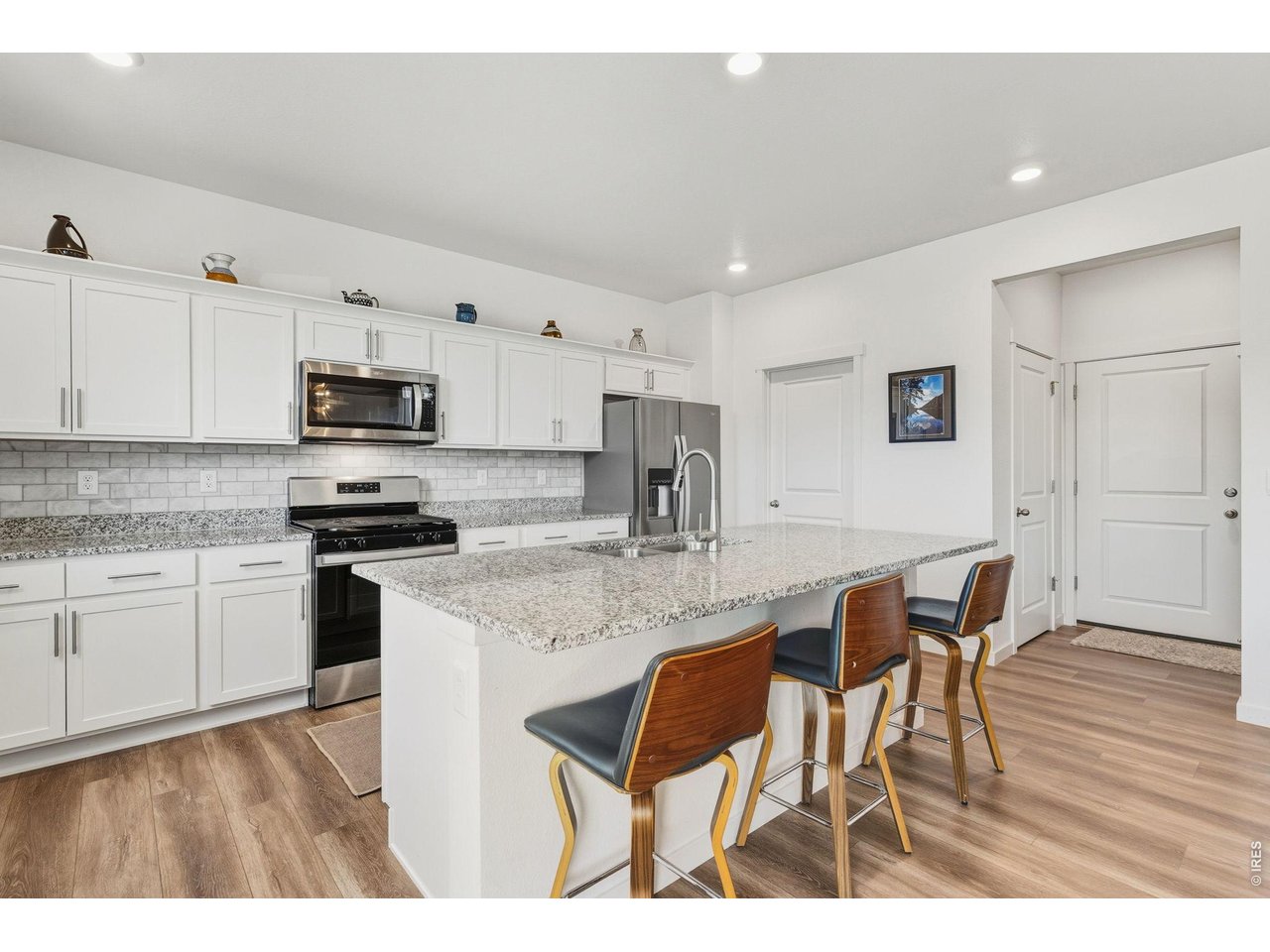 438 Bluebird Road Johnstown, CO 80534 - Photo 11 of 33 Granite countertops, white cabinetry, tile backsplash, and a large center island with breakfast-bar seating.