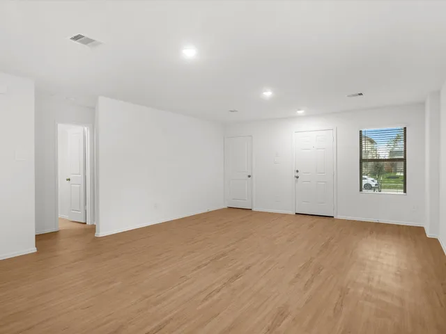 a view of an empty room with wooden floor and window