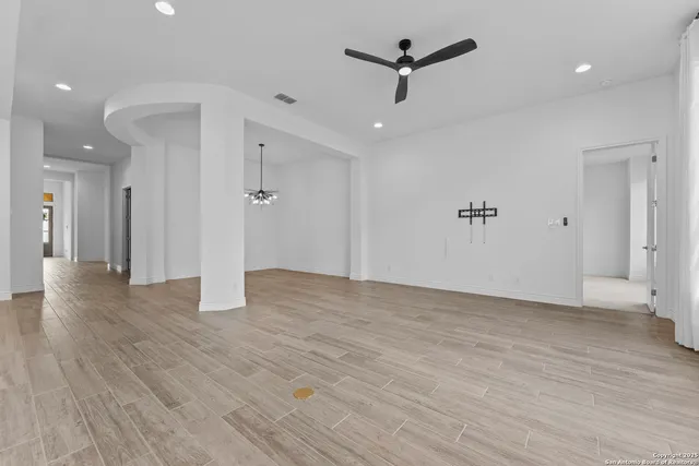a view of an empty room with wooden floor and a ceiling fan