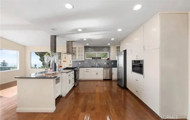 a kitchen with stainless steel appliances kitchen island granite countertop a stove a sink a refrigerator and white cabinets with wooden floor