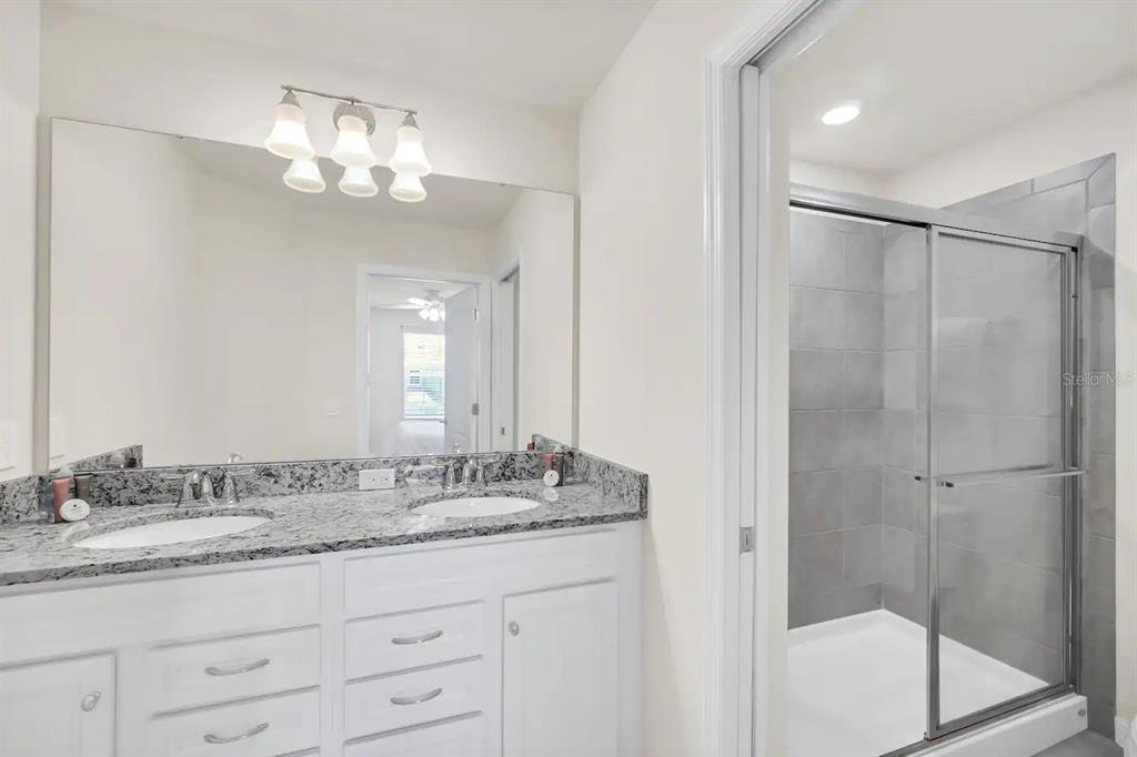 7263 Oakmoss Loop Davenport, FL 33837 - Photo 40 of 57 a bathroom with a granite countertop sink a mirror and a shower