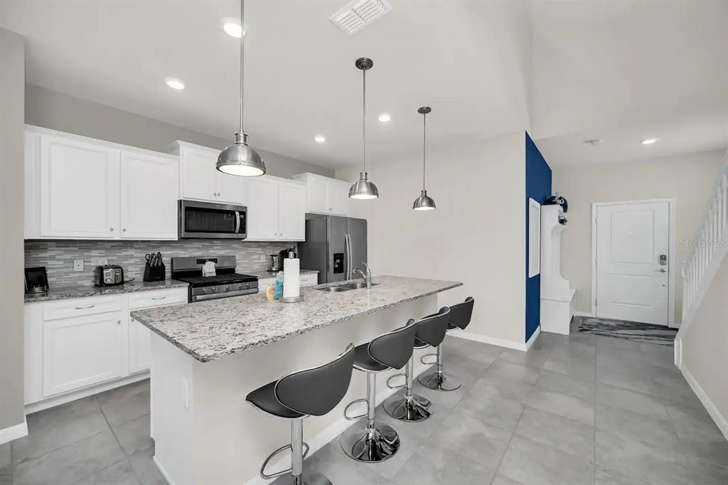 7263 Oakmoss Loop Davenport, FL 33837 - Photo 5 of 57 a kitchen with stainless steel appliances granite countertop a sink a stove a refrigerator and chairs
