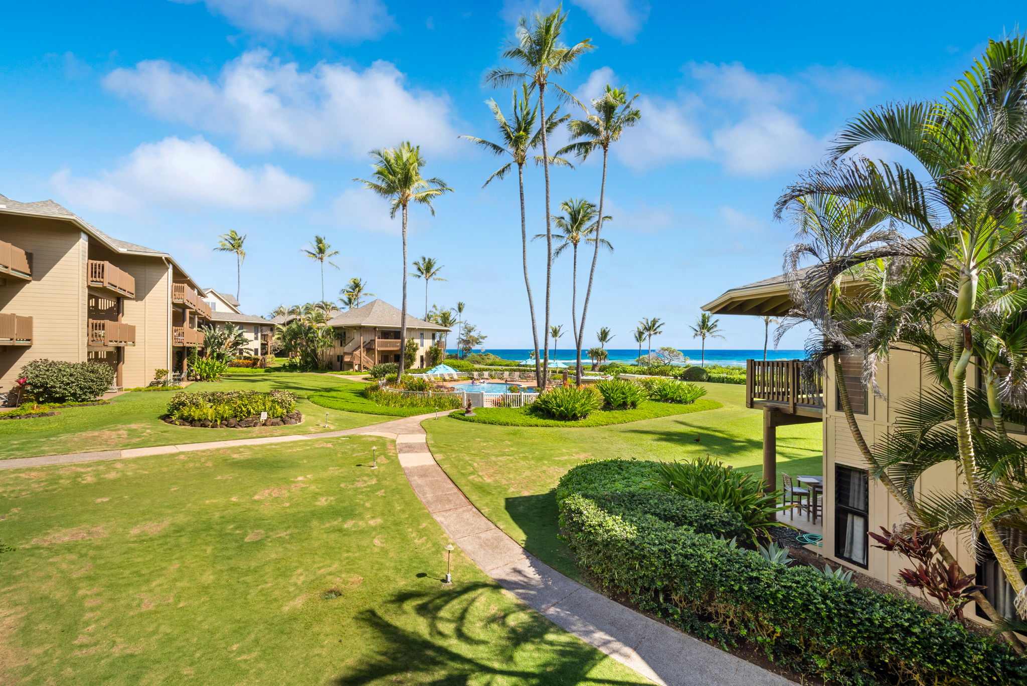 4460 Nehe Road, Unit 203 Lihue, HI 96766 - Photo 12 of 26 a view of a white house with a swimming pool and lawn chairs under an umbrella