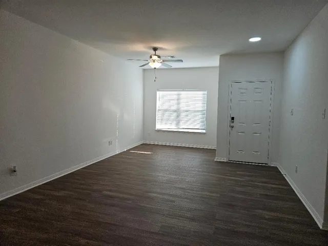 an empty room with wooden floor chandelier fan and windows