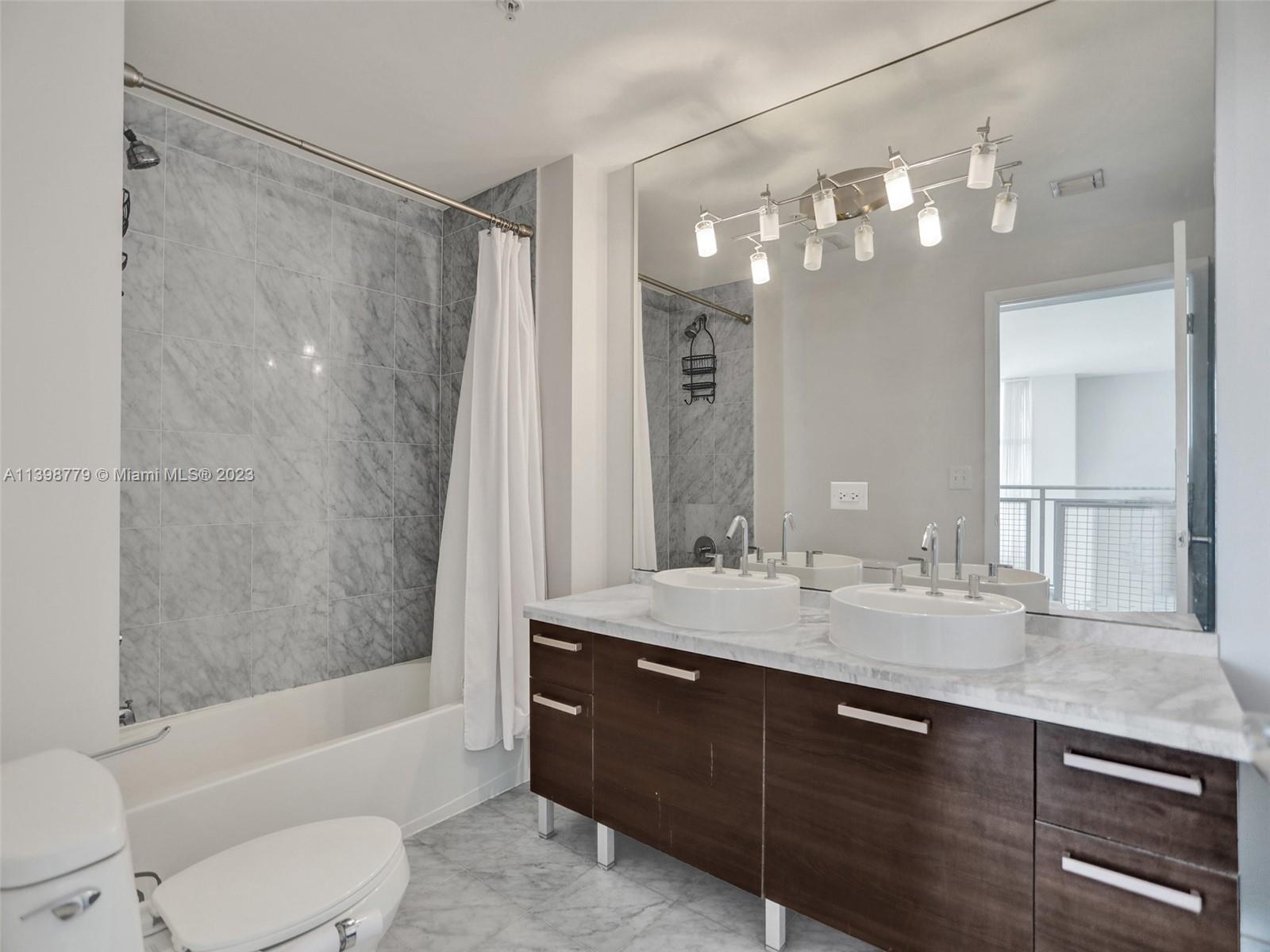 244 Biscayne Boulevard, Unit 439 Miami, FL 33132 - Photo 22 of 49 a bathroom with a granite countertop sink a toilet a mirror a bathtub and shower