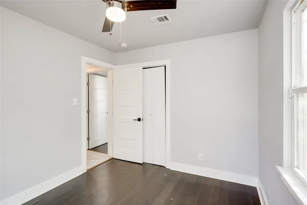 an empty room with wooden floor fan and windows