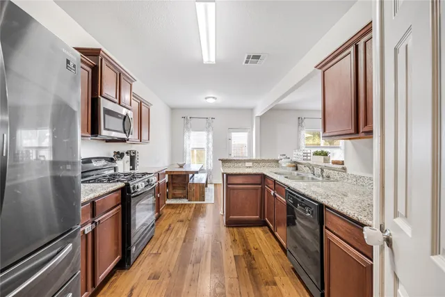 a kitchen with stainless steel appliances granite countertop hardwood floor sink stove and wooden cabinets