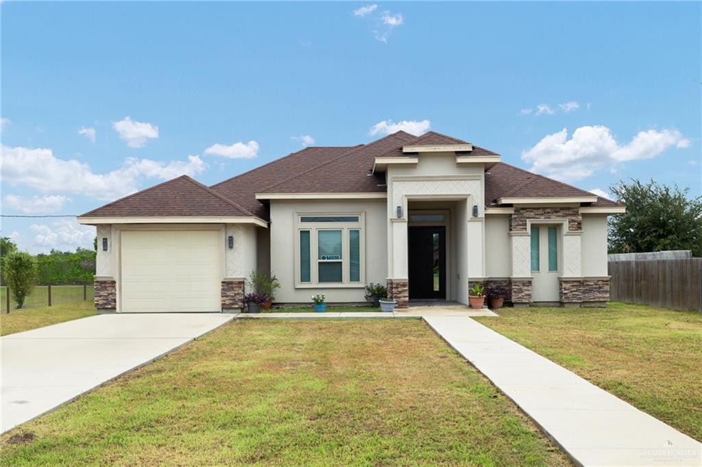 14928 East Davis Road Edcouch, TX 78538 - Photo 1 of 1 Prairie-style house with stone siding, stucco siding, a garage, a shingled roof, and concrete driveway