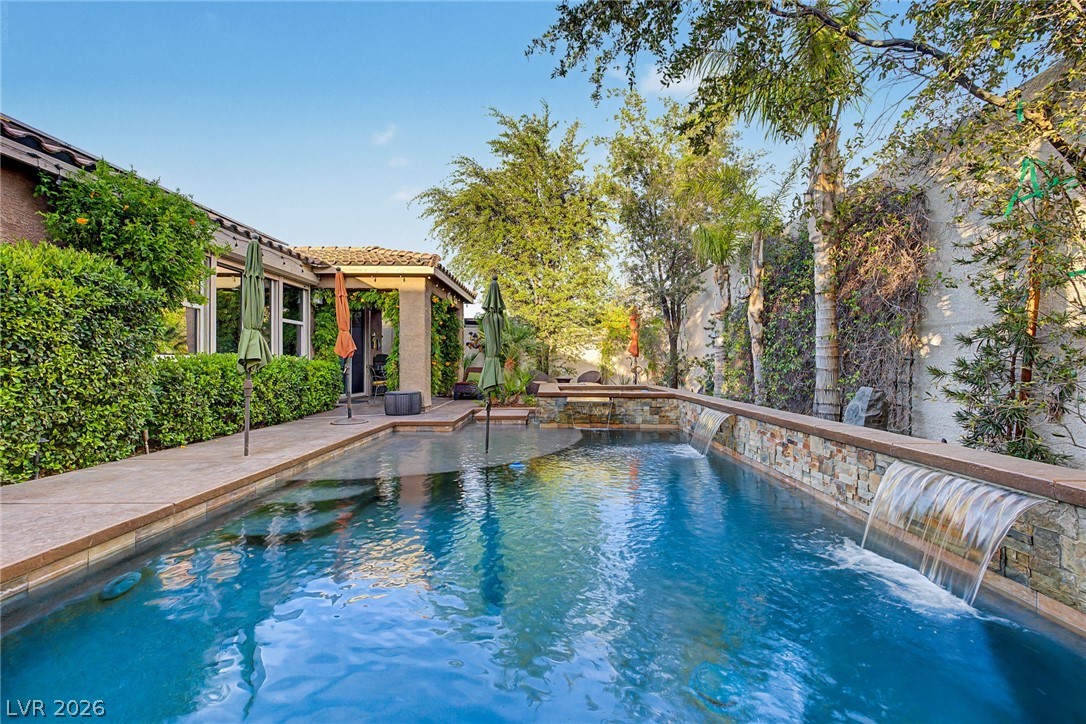 7415 Campbell Ranch Avenue Las Vegas, NV 89179 - Photo 52 of 52 An inviting backyard oasis awaits with a sparkling pool featuring elegant waterfall details and lush landscaping.