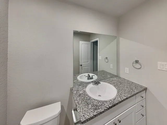a bathroom with a granite countertop sink a toilet and mirror