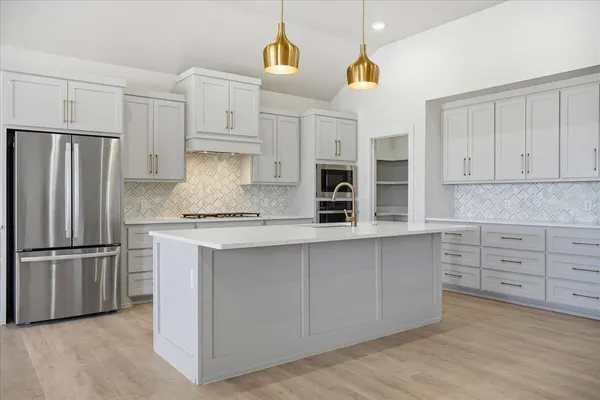 a kitchen with stainless steel appliances granite countertop a refrigerator a stove and white cabinets with wooden floors