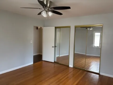 an empty room with wooden floor fan and windows