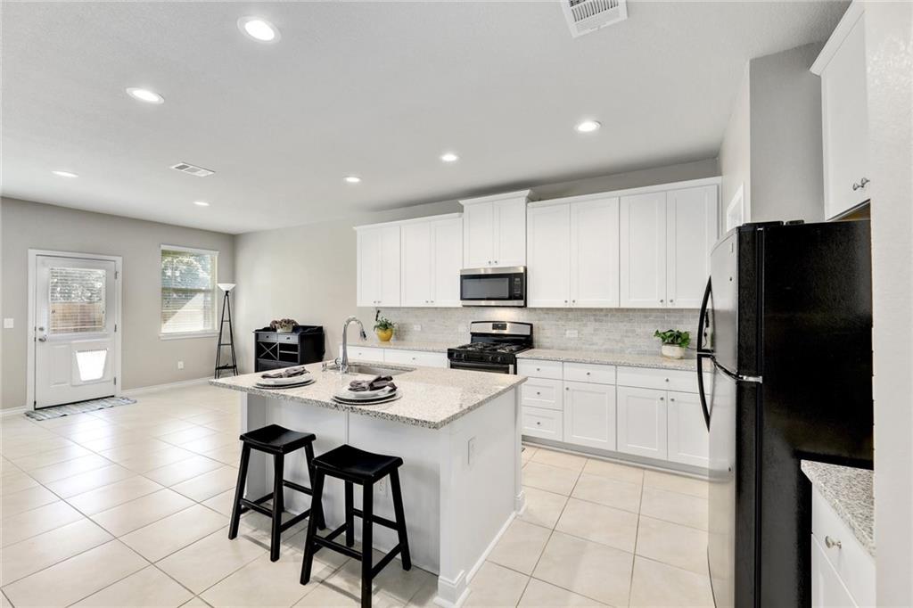 204 Tulum Terrace Leander, TX 78641 - Photo 2 of 22 Kitchen with a center island with sink, stainless steel appliances, a breakfast bar, white cabinets, and light stone countertops