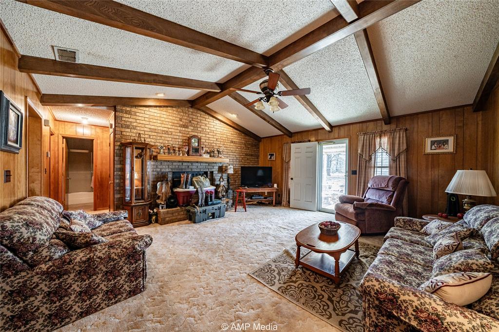 1992 Sand Flat Road Jacksboro, TX 76458 - Photo 30 of 36 Carpeted living room featuring a fireplace, wooden walls, a textured ceiling, and vaulted ceiling with beams
